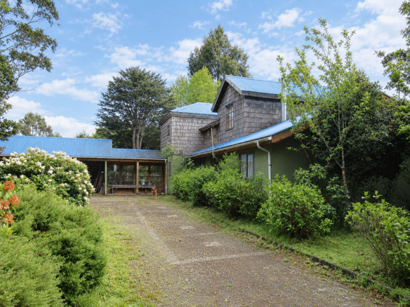 Casa de madera con techo azul y camino de acceso entre jardines en parcela de Panitao, Puerto Montt