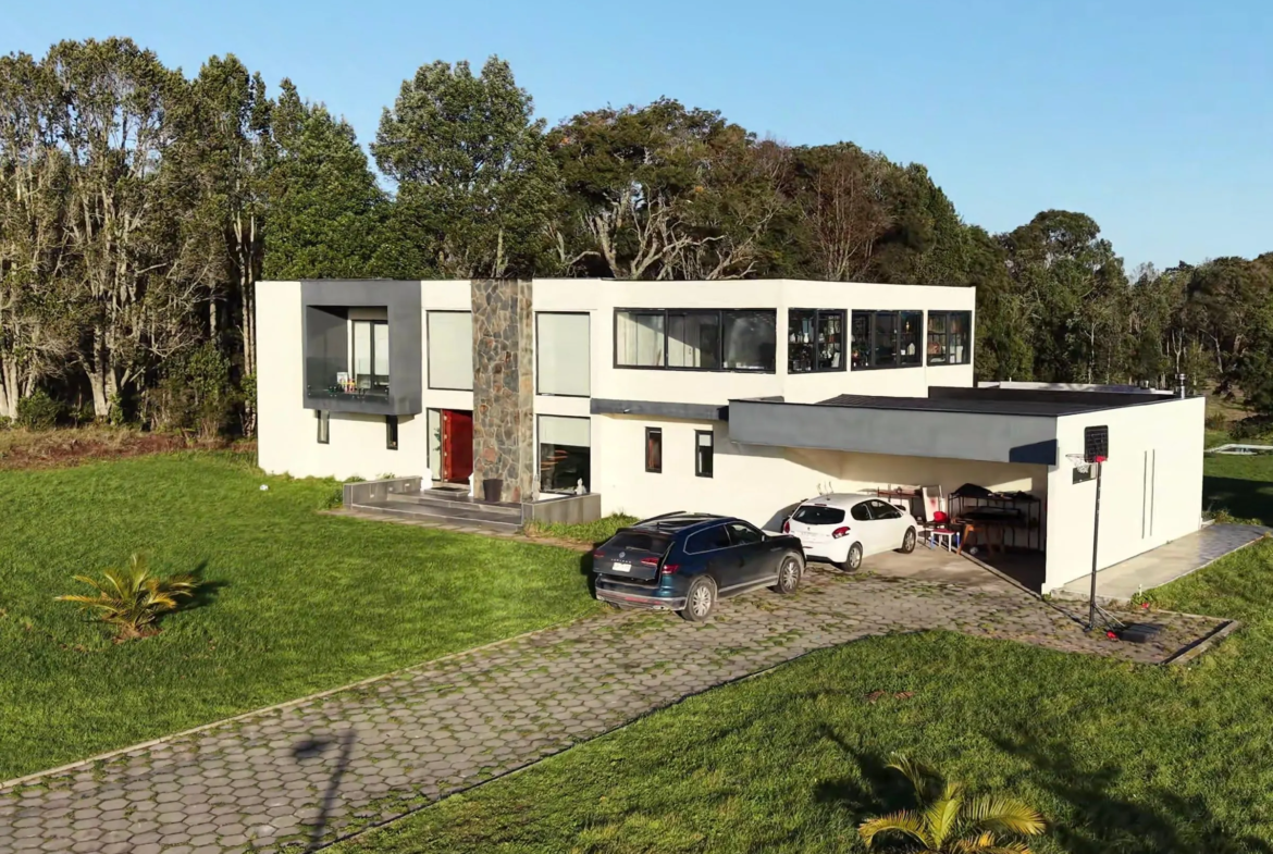 Casa de dos pisos con estacionamiento techado y acceso adoquinado, vista lateral