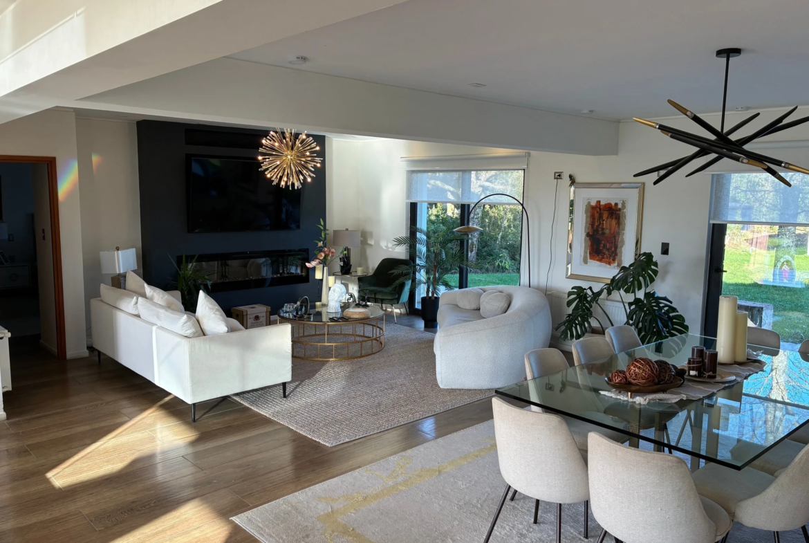 Living con chimenea eléctrica, sofás blancos y comedor de vidrio con luz natural